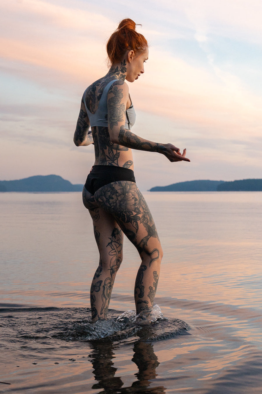 Woman with tattoos standing in water at sunset